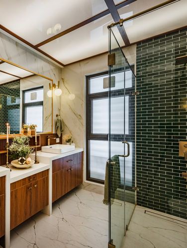 Bathroom with marble walls, wood vanity, brass fixtures and dark green tiled glass shower
