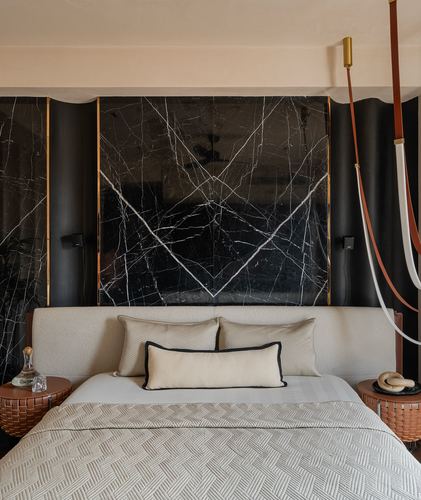 Bed with beige boucle headboard against bookmatched black marble panel wall with brass trim