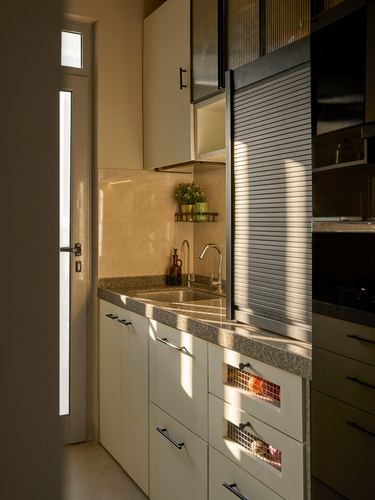 Sunlit galley kitchen with stone counter, sink, and roller shutter cabinet above