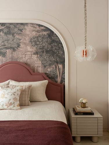 Arched alcove bed with mauve velvet headboard, mural wallpaper, and sculptural pendant beside a ribbed nightstand