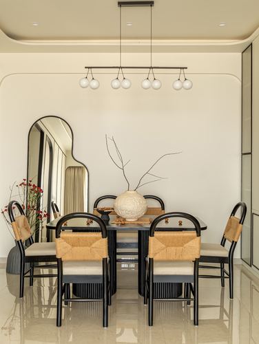 Dining table with black wood chairs featuring woven rust seat backs beneath a globe pendant light