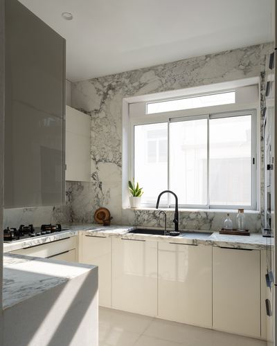 White marble-clad kitchen corner with glossy cream cabinets and black tap under a bright window