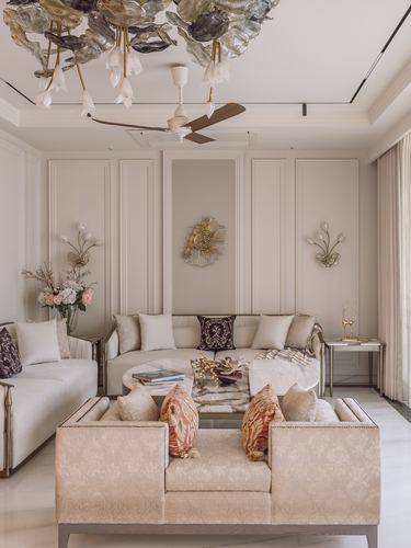 Cream living room with paneled walls, curved sofa, and ornate glass chandelier above a ceiling fan