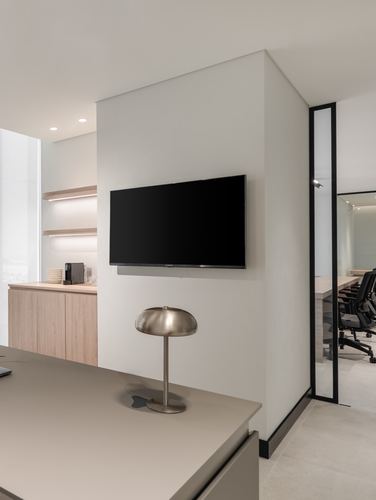 Minimalist office pantry with wall-mounted tv, oak cabinetry, and glass partition to meeting room beyond