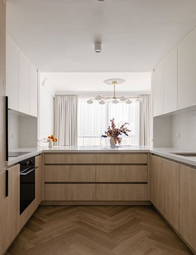 White and light wood U-shaped kitchen with herringbone floor and brass pendant light over window