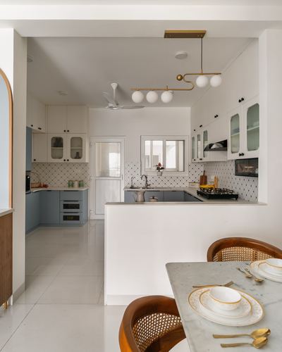 U-shaped white and blue kitchen with patterned tile backsplash, seen past a marble dining table