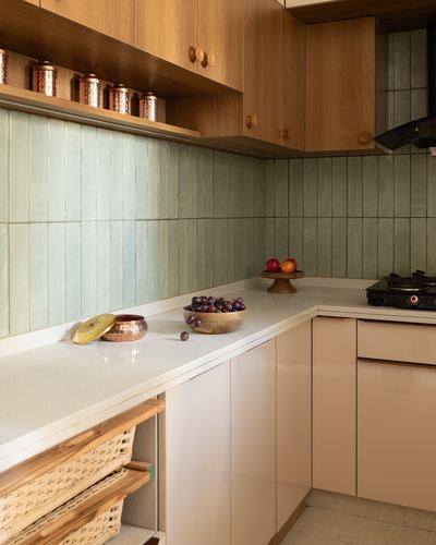 Corner kitchen counter with ribbed green tile backsplash, wood cabinets, copper vessels and cane baskets