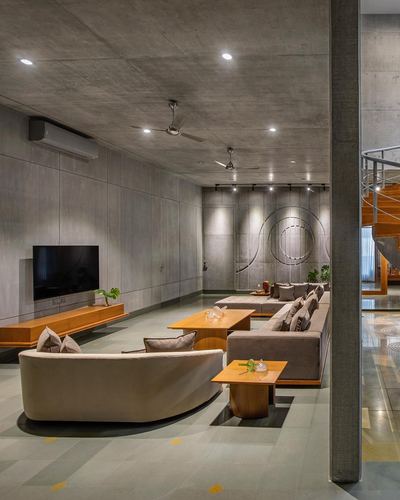 Long concrete living room with curved bench, sectional sofa, wall-mounted tv and circular metal wall art