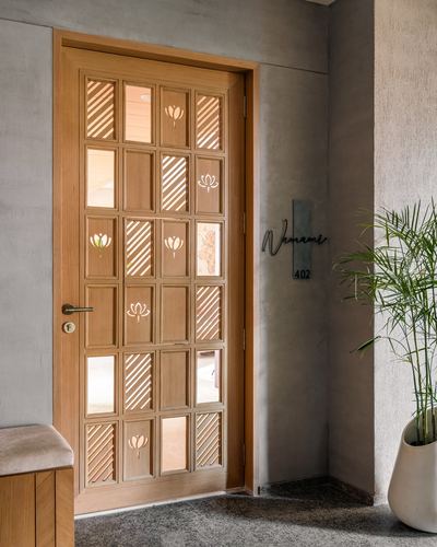 Wooden entrance door with lotus cutout panels beside a textured grey wall and potted plant
