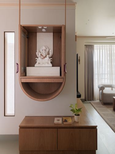 Suspended wooden pooja cabinet with white idol above a wooden console in a pink-toned hallway