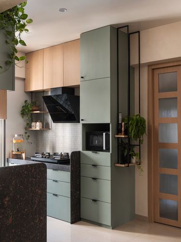 Sage green kitchen cabinetry with black steel plant shelving unit beside wooden panelled door
