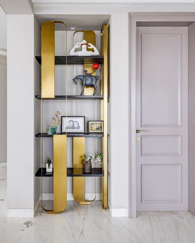 Brass-framed black shelving unit in a wall niche displaying decor pieces beside a paneled door