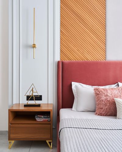 Bedroom corner with pink velvet headboard, diagonal wood panel, wooden nightstand and gold wall sconce