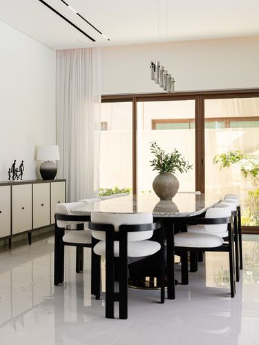White marble dining table with black curved chairs beneath a linear pendant light near glass doors