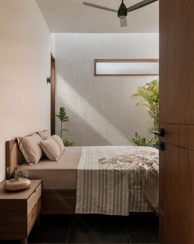 Sunlit bedroom with cane headboard bed, wooden door open to a small planted courtyard