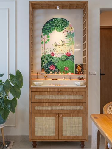 Wooden pooja cabinet with cane doors and a painted arched mural niche with brass idols