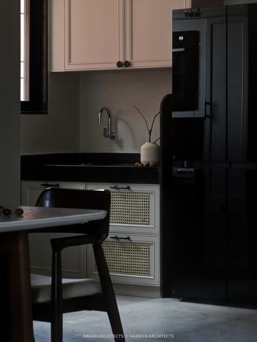 Kitchen corner with cream cabinetry, cane drawer fronts, black countertop, and dark tall appliance panel in low light