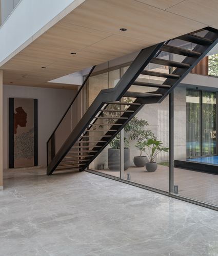 Black steel floating staircase beside glass wall overlooking courtyard with potted plants and pool, Ahmedabad home