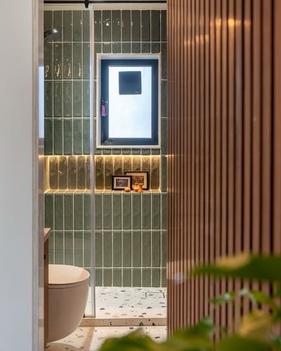 View through fluted wood panels into a green-tiled bathroom with backlit niche and terrazzo floor