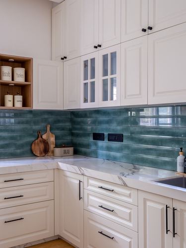 Corner of a cream cabinetry kitchen with teal ribbed tile backsplash and white stone countertop