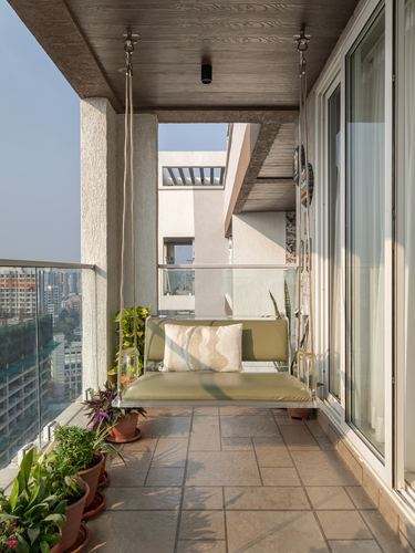 Balcony with a hanging swing, olive cushions, potted plants and a city skyline view
