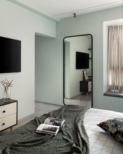 Sage green bedroom with leaning mirror reflecting a TV console and window seat nook