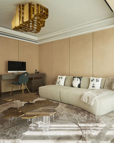 Beige sectional sofa with face-print cushions beside brass coffee tables under a geometric brass chandelier