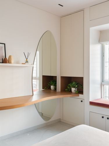 Curved wooden vanity counter with oval mirror against beige built-in wardrobe near window seat