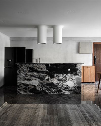 Kitchen island in bold black-and-white veined marble beneath two cylindrical pendant lights