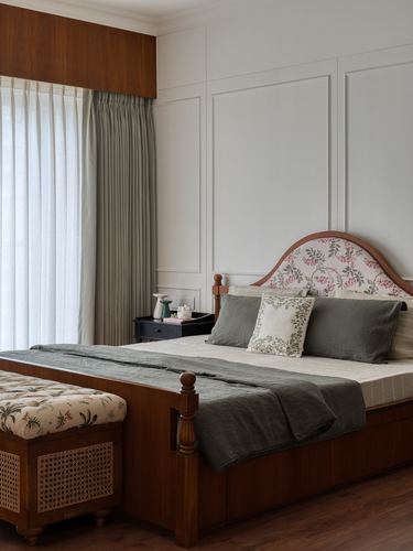 Wood bed with floral upholstered headboard, sage linens, cane bench, panelled wall, sheer curtains
