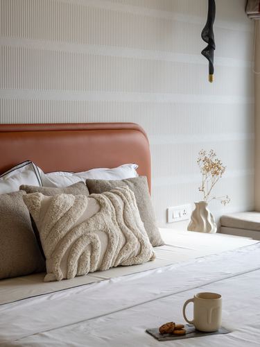 Bed with terracotta leather headboard, textured cushions, ceramic vase and pendant light beside window