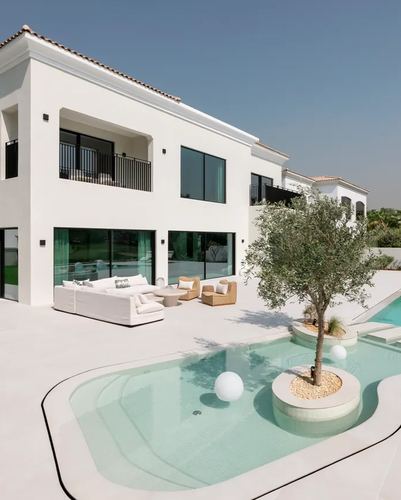 White contemporary Dubai villa exterior with curved pool, central olive tree island, and outdoor lounge seating.