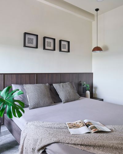 Bedroom with dark wood headboard, patterned pillows, gray linens, framed art trio, and pendant light
