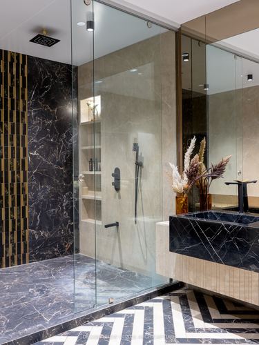 Luxury bathroom with black marble vanity, glass shower, and chevron marble flooring