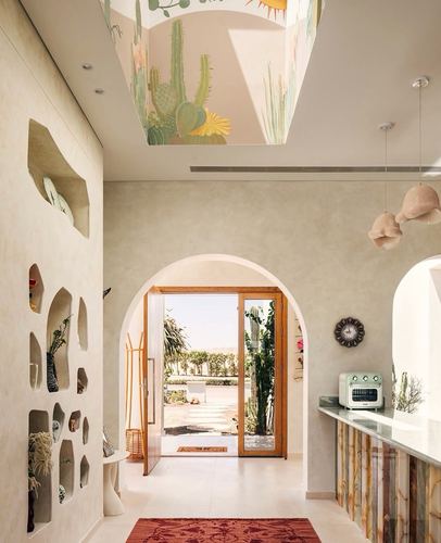 Plastered hallway with sculpted niches leading through an arch to a sunlit terrace, painted ceiling mural above