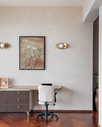 Study nook with floating wood desk, upholstered chair, brass sconces and botanical art on lime-plastered wall