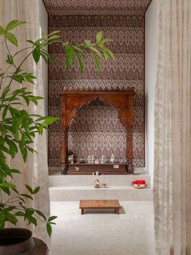 Carved wooden pooja mandir set in patterned niche with marble platform and sheer curtains