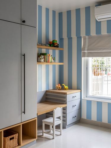 Child's study nook with blue and white striped wall, wooden desk, and white chair
