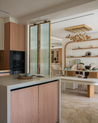 Kitchen island with wood cabinetry beside reeded glass doors opening to sunlit marble-floored dining area