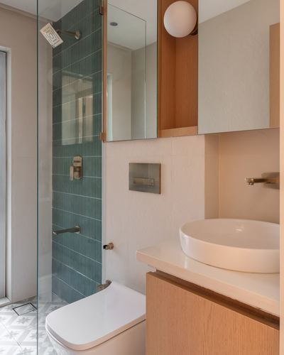 Small bathroom with teal ribbed tile shower, wood vanity, round vessel sink, patterned floor