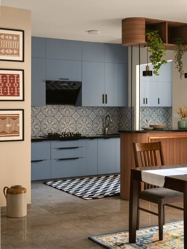 Blue kitchen cabinetry with patterned tile backsplash, wood breakfast counter, and hanging plants beside dining table