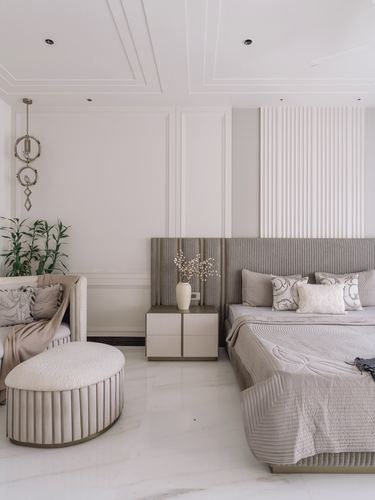 Neutral-toned bedroom with fluted headboard wall, marble floor, round ottoman and layered paneled ceiling