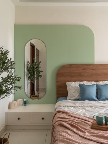 Bedroom with sage green curved wall, wood headboard, blue and pink linens, oval mirror