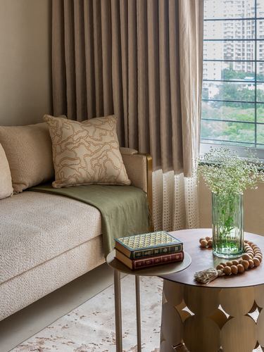 Beige boucle sofa corner with patterned cushion, brass side table, and city view through sheer curtains