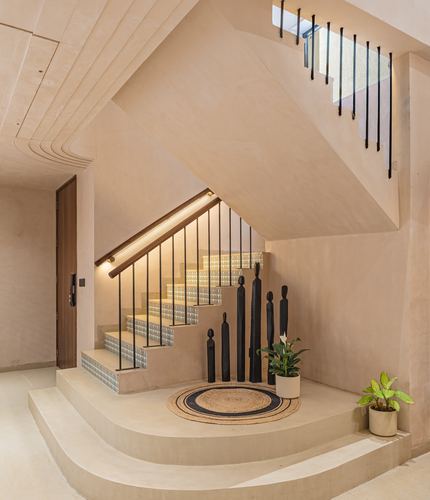 Curved plaster staircase with wooden handrail, black totem sculptures and jute rug in entry foyer