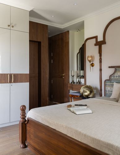 Bedroom with carved arched wooden headboard, brass sconce, and glossy white wardrobe with wood inlay