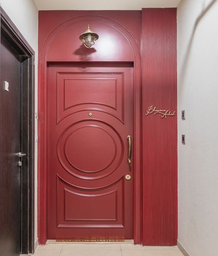 Deep red arched entrance door with circular paneling and brass lantern above