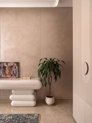 Beige plastered foyer with sculptural white console, potted plant, and fluted wardrobe door