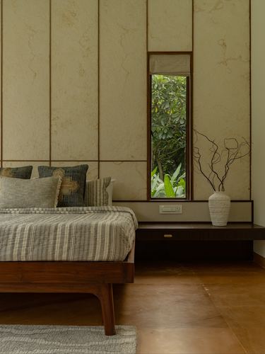 Bedroom with textured stone wall panels, wooden bed, floating console and narrow window framing greenery