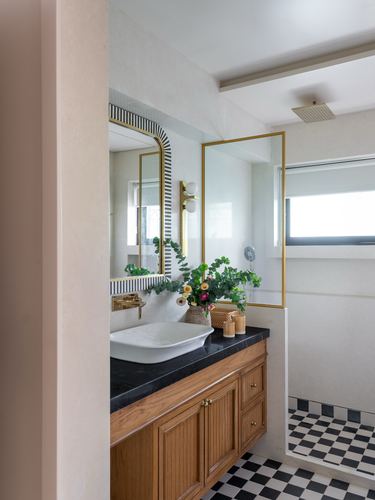 Bathroom with wood vanity, black stone counter, oval sink, arched brass mirror, checkerboard floor